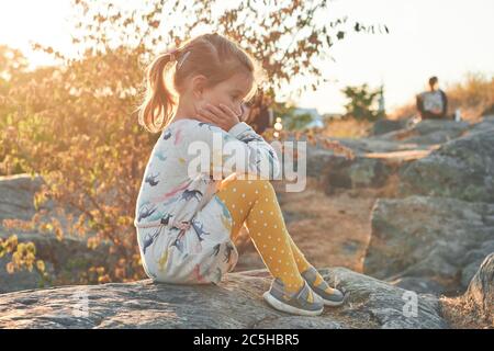 Sad girl sitting on stones, sunset on background Stock Photo