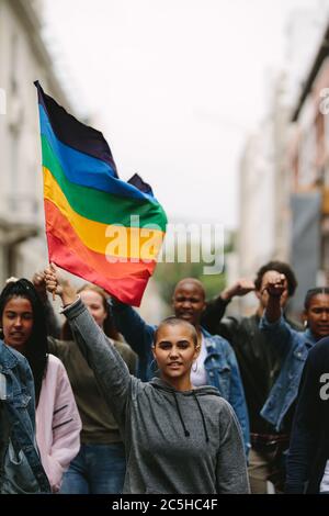 Female holding the gay rainbow flag at the Gay Pride Parade in city. Supporters and members of LGBTQI community during a Queer Pride Parade. Stock Photo