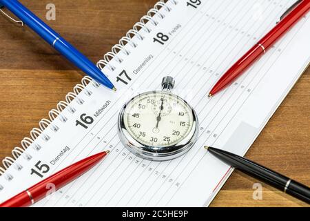 Pens lying on schedule and pointing towards stopwatch (with captions of the days of the week in German) Stock Photo