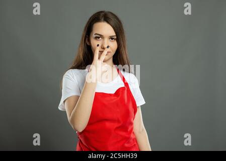 Portrait of female supermarket employee making look at me gesture on gray background Stock Photo