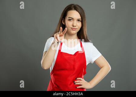 Portrait of female supermarket employee making watching you gesture on gray background Stock Photo
