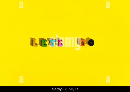 Flatlay of wood multicolored letters is inscription of lets go with shadows on bright plain yellow background. wishes and messages made up of models Stock Photo