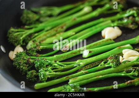 Cooking broccolini in a fried pan. Angle view, closeup. Stock Photo