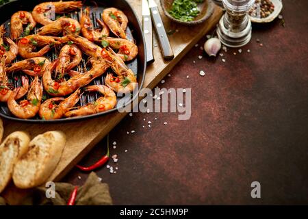 Grilled prawns in cast iron grilling pan with fresh lemon, parsley, chili, garlic white wine sauce Stock Photo