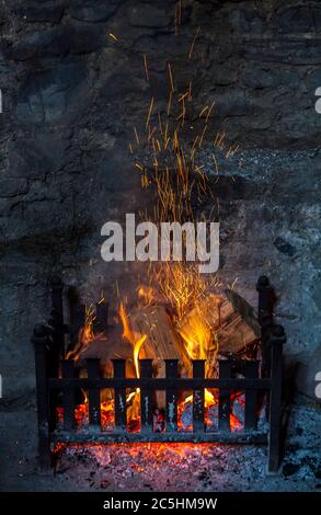 Old fashioned open log fireplace in with flames and sparks Stock Photo