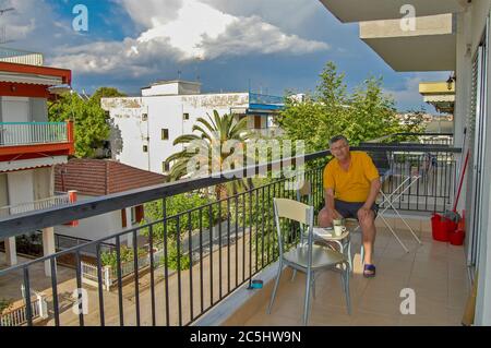 A tourist in Greece sits on a high terrace and drinks morning coffee. Traditional coffee before going to the beach. Stock Photo