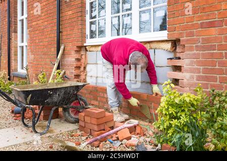 BUCKINGHAM, UK - March 15, 2016. Bricklayer building a wall on a UK heritage house while installing replacement wooden windows. Home improvement, prop Stock Photo