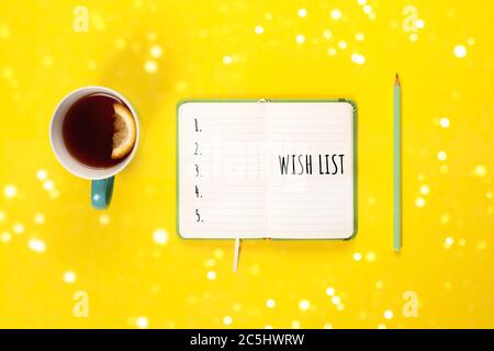 Wish list. Mint Tea cup and modern notebook with to do list on bright yellow desk from above, planning or Holiday present concept. Top view, flat lay, Stock Photo