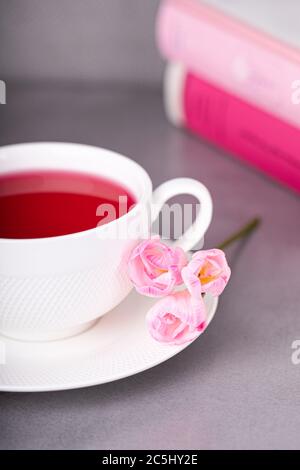 Raspberry tea, pink freesia flowers and books on a gray background Stock Photo