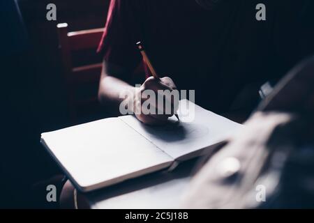 Young boy's hand sketching on a drawing book using traditional lead pencil, graphite core pencil, using the afternoon light from a window. Stock Photo