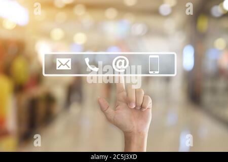 Hand pressing a contact us icons on blur office lights background. Stock Photo