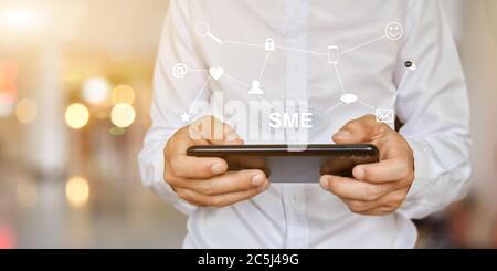 Businessman hand using mobile smartphone with SME icon on virtual screen. Idea for Small and medium-sized enterprises business Stock Photo