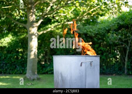 Close of a home made metal garden incinerator seen burning general household, non toxic water in a garden setting. Stock Photo