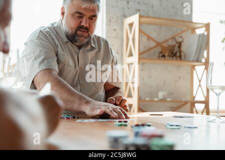 Shuffling. Two happy mature friends playing cards and drinking wine. Look delighted, excited. Caucasian men gambling at home. Sincere emotions, wellbeing, facial expression concept. Good old age. Stock Photo