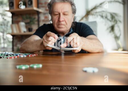 Exciting. Happy mature man playing cards and drinking wine with friends. Looks delighted, excited. Caucasian man gambling at home. Sincere emotions, wellbeing, facial expression concept. Good old age. Stock Photo