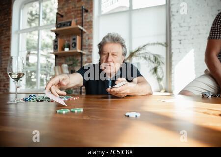 Exciting. Happy mature man playing cards and drinking wine with friends. Looks delighted, excited. Caucasian man gambling at home. Sincere emotions, wellbeing, facial expression concept. Good old age. Stock Photo