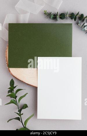 Wedding invitation and olive green envelope mockup in a gray background with eucalyptus leaves Stock Photo