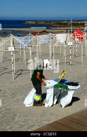 3rd July 2020, Vila Praia de Ancora, northern Portugal: A local government worker puts out bin bags on the beach in preparation for the start of the tourist season. Stock Photo