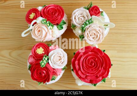 Top view of four cupcakes with gorgeous red and pink flower shaped frosting on wooden table Stock Photo