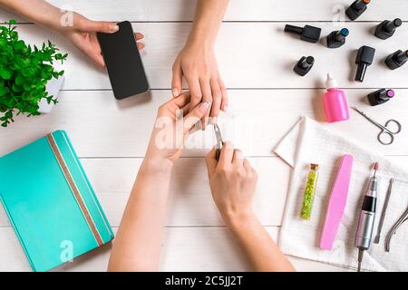 Manicure for the client. Close-up of the hands of a manicurist and client on a wooden background Stock Photo