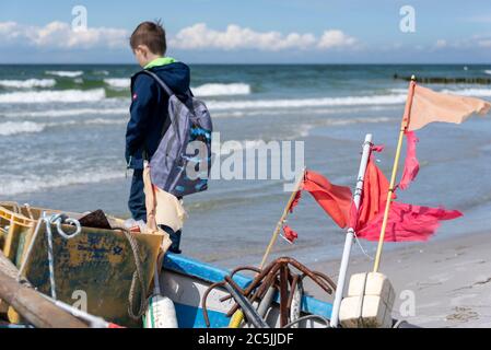 Hiddensee, Germany. 05th June, 2020. A boy with a backpack stands behind a small fishing boat at the sea. Credit: Stephan Schulz/dpa-Zentralbild/ZB/dpa/Alamy Live News Stock Photo