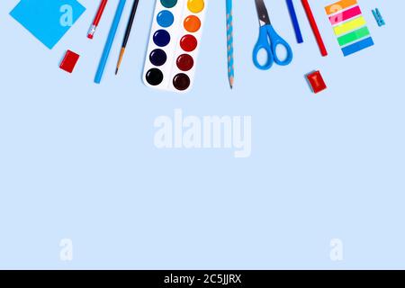Back to school picture with blue and red pencils, paper clips, scissors and watercolor on blue background. Stock Photo