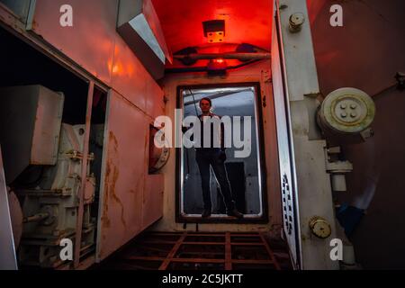 Man in gateway corridor of airlock of abandoned bunker. Big hermetic door illuminated by red lantern Stock Photo