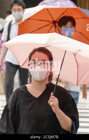 Tokyo, Japan. 3rd July, 2020. Pedestrians wearing face masks hold umbrellas during the rainy season (Tsuyu) at the Ginza shopping area. Tokyo reported 124 new coronavirus cases on Friday, the highest number for a single day in the capital since May. Credit: Rodrigo Reyes Marin/ZUMA Wire/Alamy Live News Stock Photo