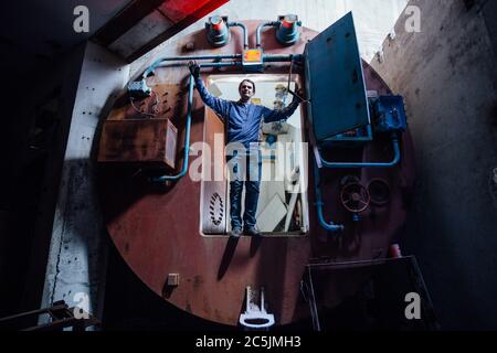 Man in gateway corridor of airlock of abandoned bunker. Big hermetic door illuminated by red lantern Stock Photo