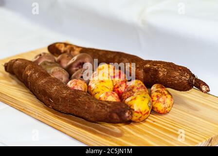 Raw yucca on the wooden table, Manihot esculenta. (Cassava raw tuber) with regional potatoes from the Andes at a market in Peru, Bolivia, Argentina, s Stock Photo