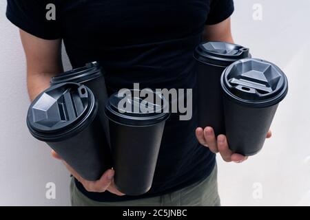 Caucasian man brings at hands coffee in black paper cups with black lids,no face Stock Photo