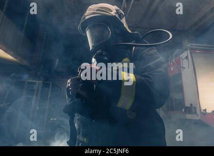 Portrait of a fireman wearing firefighter turnouts and helmet. Dark background with smoke and blue light. Stock Photo