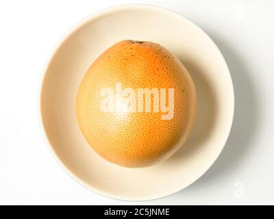 A whole pink grapefruit in a bowl centred on a white background Stock Photo