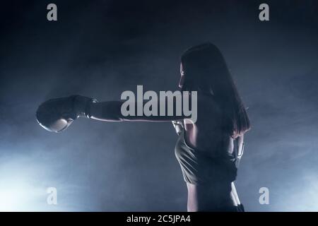 Side view of a silhouette young woman with boxing gloves making a direct hit. Stock Photo