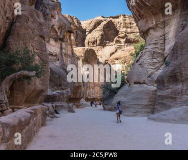 Jordan, Petra, Tourists hike into a narrow slot canyon called the Siq to see the ruins of the Nabataean city of Petra in the Petra Archeological Park is a Jordanian National Park and a UNESCO World Heritage Site. Stock Photo