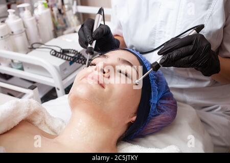 The beautician performs the microcurrent procedure in the beauty salon. The procedure stimulates collagen production, lifting, fights wrinkles, facial Stock Photo