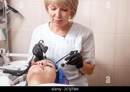 The beautician performs the microcurrent procedure in the beauty salon. The procedure stimulates collagen production, lifting, fights wrinkles, facial Stock Photo