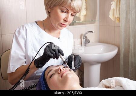 The beautician performs the microcurrent procedure in the beauty salon. The procedure stimulates collagen production, lifting, fights wrinkles, facial Stock Photo