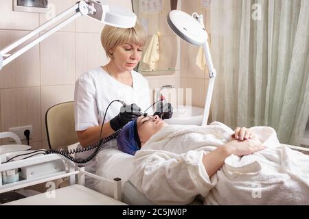 The beautician performs the microcurrent procedure in the beauty salon. The procedure stimulates collagen production, lifting, fights wrinkles, facial Stock Photo