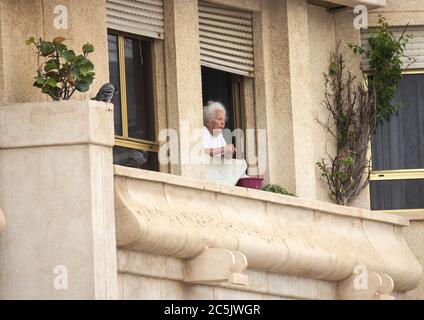 Elderly woman looking out of apartment window in Spain. Stock Photo