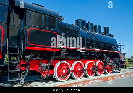 Old Russian (Soviet) steam locomotive on a pedestal on a background of blue sky Stock Photo