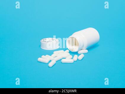 White medicine pills tablets capsules spilled out of pill bottle on a blue background with copy space and room for text Stock Photo