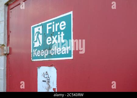 Shallow focus of an old Fire Exit and No Smoking sign seen attached for a fire door, used for emergency exit for a warehouse and logistics company. Stock Photo