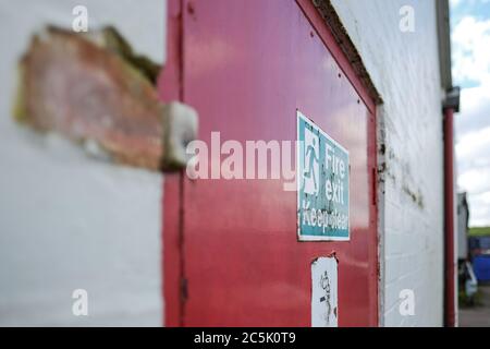 Shallow focus of an old Fire Exit and No Smoking sign seen attached for a fire door, used for emergency exit for a warehouse and logistics company. Stock Photo