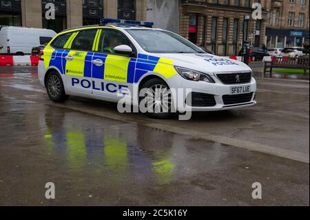 Glasgow, Scotland, UK. 3rd July, 2020. Pictured: A police car makes a reflection against the wet concrete of George Square. Buchanan Street shopping area with shoppers braving the pouring rain using umbrellas and face coverings which will become mandatory on 10th July next week. Credit: Colin Fisher/Alamy Live News Stock Photo