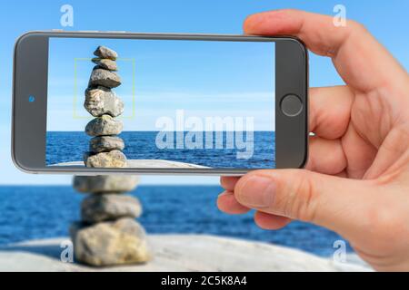 Stacked Rocks balancing, stacking with precision. Stone tower on shore. Photo smartphone. Smartphone in hand. Stone pyramid on screen. Stock Photo