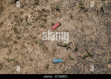 Used and empty shotgun shells from a rifle left and discarded laying on the dirt smashed and buried in the ground Stock Photo