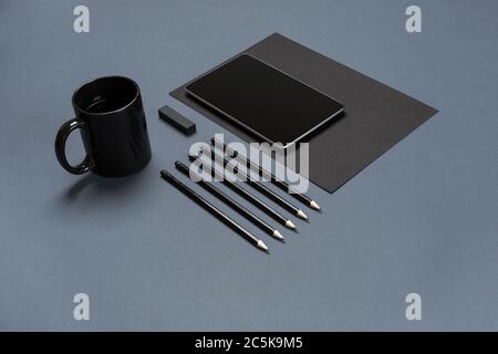 Flat lay of blank black paper sheet, black stationery items and coffee cup on gray desktop. Mock up Stock Photo