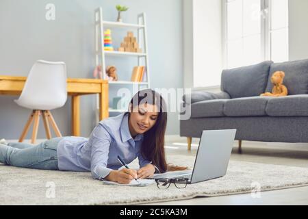 Work from home. Beautiful woman taking notes during online business conference or educational class on laptop in room Stock Photo