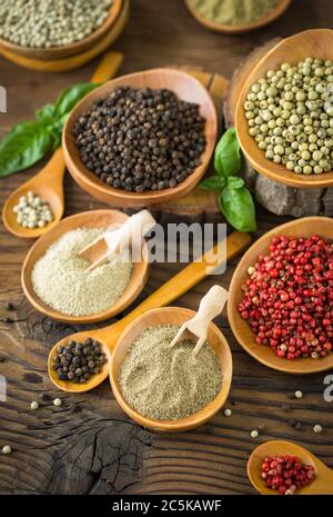 Various colorful peppercorns in the bowls and spoons on wooden table. Stock Photo